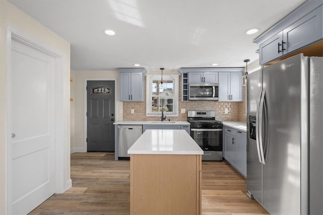 kitchen with sink, light wood-type flooring, a center island, stainless steel appliances, and decorative light fixtures