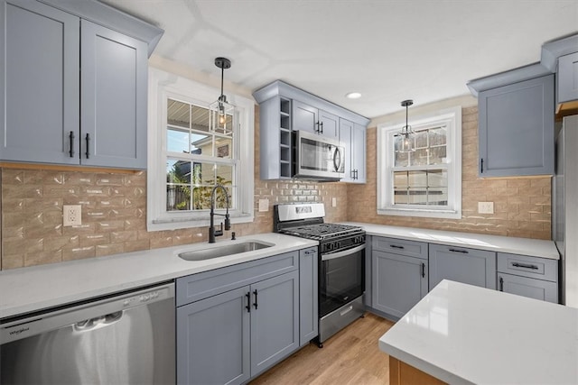 kitchen with tasteful backsplash, appliances with stainless steel finishes, light hardwood / wood-style flooring, sink, and decorative light fixtures