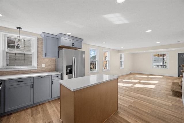 kitchen with a kitchen island, gray cabinetry, stainless steel fridge with ice dispenser, light hardwood / wood-style floors, and tasteful backsplash