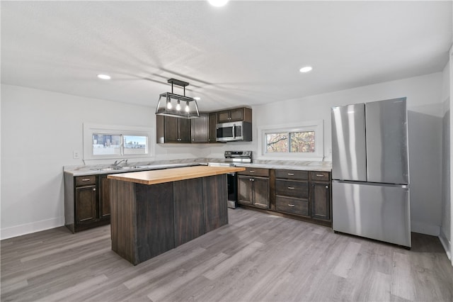 kitchen with a center island, light hardwood / wood-style floors, stainless steel appliances, pendant lighting, and wooden counters