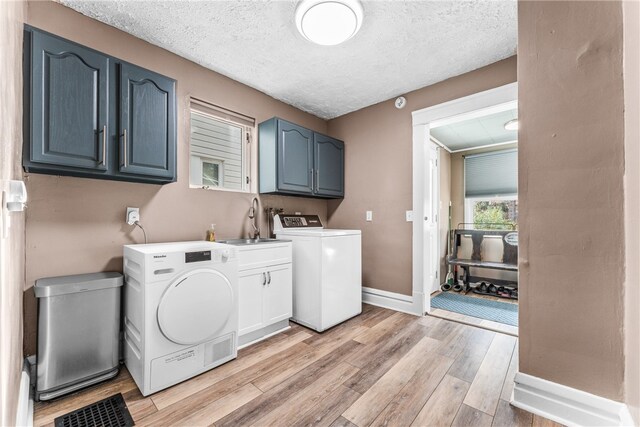 clothes washing area featuring sink, a textured ceiling, light hardwood / wood-style floors, and cabinets