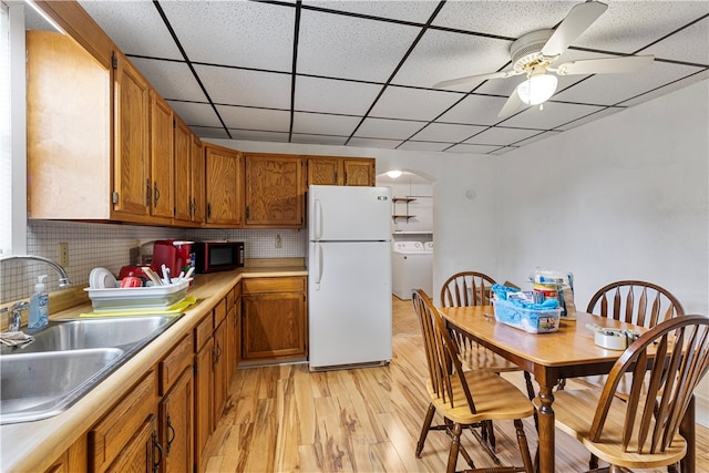 kitchen with washer / dryer, backsplash, sink, light wood-type flooring, and white fridge