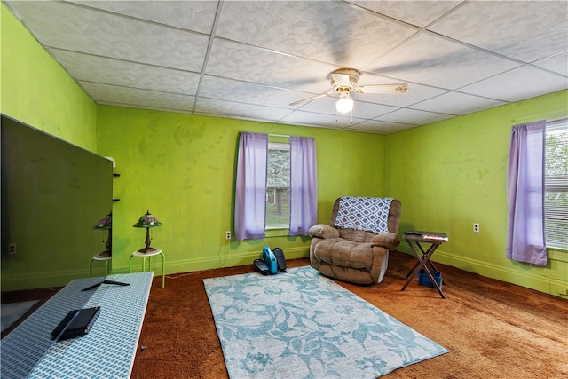 living area with ceiling fan, a drop ceiling, and carpet floors