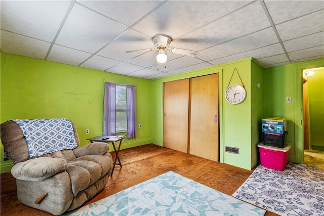 living area with carpet, a paneled ceiling, and ceiling fan