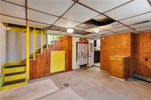 basement with a drop ceiling and wood walls