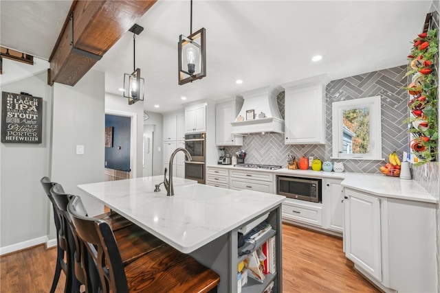 kitchen with white cabinets, hanging light fixtures, appliances with stainless steel finishes, a kitchen breakfast bar, and a kitchen island with sink