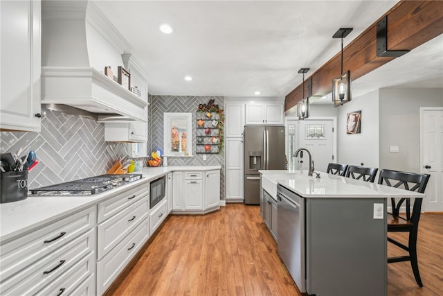 kitchen featuring a breakfast bar area, appliances with stainless steel finishes, white cabinetry, light wood-type flooring, and pendant lighting