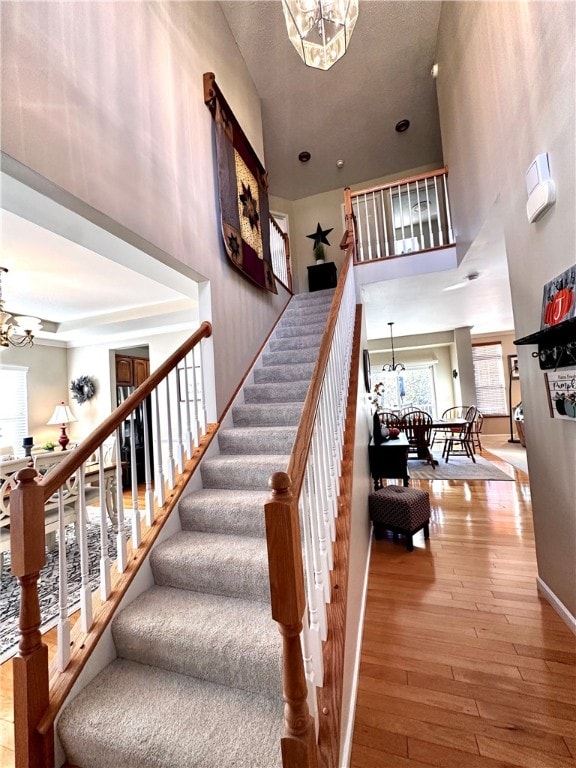 stairs featuring a high ceiling, hardwood / wood-style flooring, and an inviting chandelier