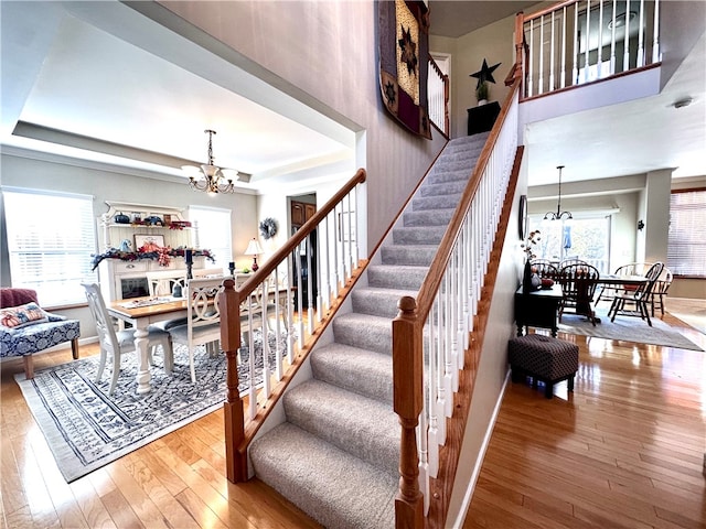 staircase featuring hardwood / wood-style flooring, an inviting chandelier, and a raised ceiling