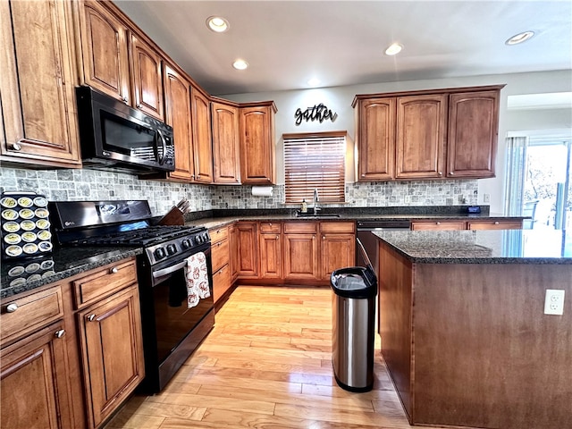 kitchen with dark stone countertops, light hardwood / wood-style floors, tasteful backsplash, and black appliances