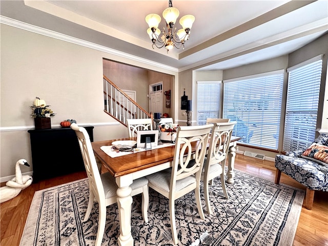 dining space with ornamental molding, hardwood / wood-style flooring, a chandelier, and a tray ceiling