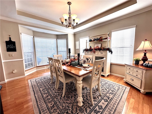 dining space featuring light hardwood / wood-style flooring, a notable chandelier, a tray ceiling, and a wealth of natural light