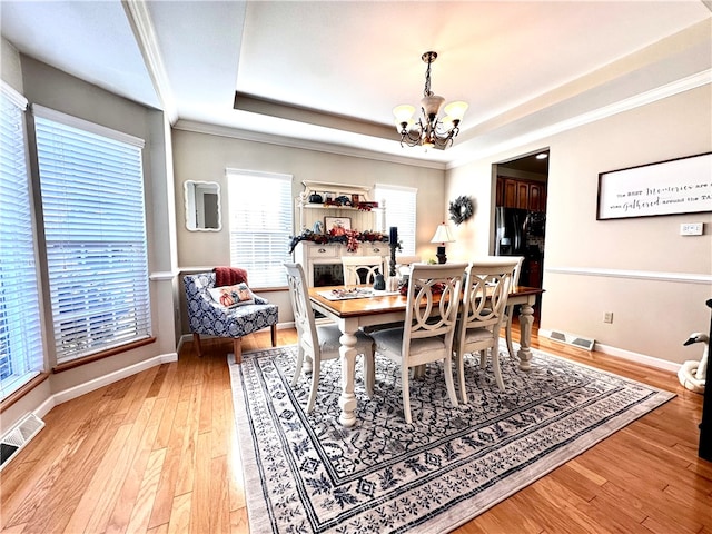 dining space featuring ornamental molding, light hardwood / wood-style flooring, a notable chandelier, and a raised ceiling