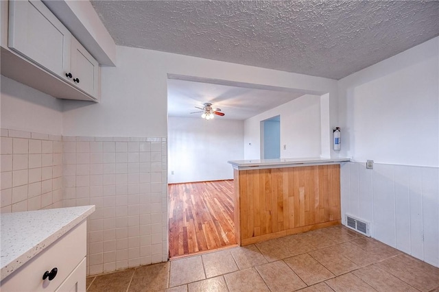 kitchen featuring tile walls, ceiling fan, kitchen peninsula, and white cabinets