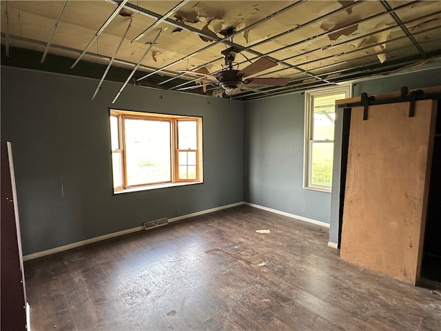 spare room featuring dark wood-type flooring, a barn door, and a healthy amount of sunlight