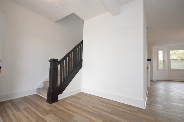 stairs featuring beam ceiling, a textured ceiling, and hardwood / wood-style flooring