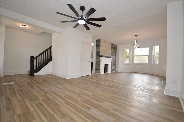 unfurnished living room featuring a stone fireplace, a textured ceiling, light hardwood / wood-style floors, and ceiling fan