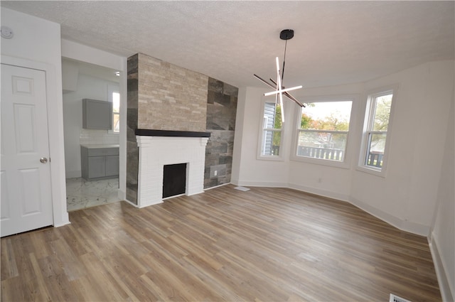 unfurnished living room with an inviting chandelier, a textured ceiling, hardwood / wood-style flooring, and a large fireplace