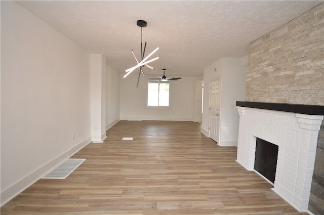 unfurnished living room with a textured ceiling, light hardwood / wood-style flooring, and ceiling fan with notable chandelier