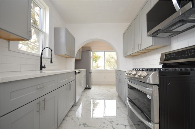 kitchen with appliances with stainless steel finishes, gray cabinetry, a wealth of natural light, and backsplash