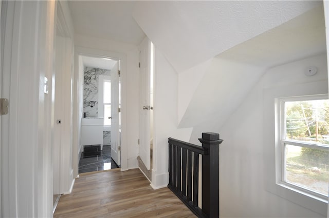 hallway with light hardwood / wood-style floors, a textured ceiling, and vaulted ceiling