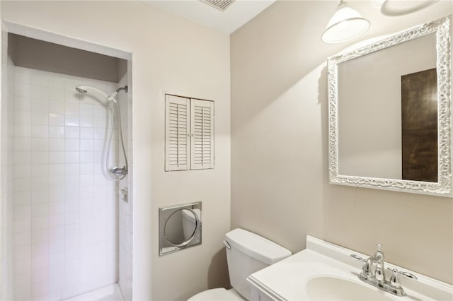 bathroom featuring vanity, a tile shower, and toilet