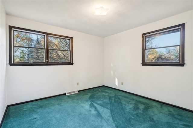 unfurnished room featuring dark carpet and a wealth of natural light