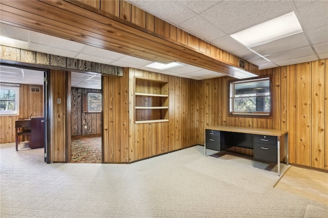 basement featuring light carpet, wood walls, and a paneled ceiling