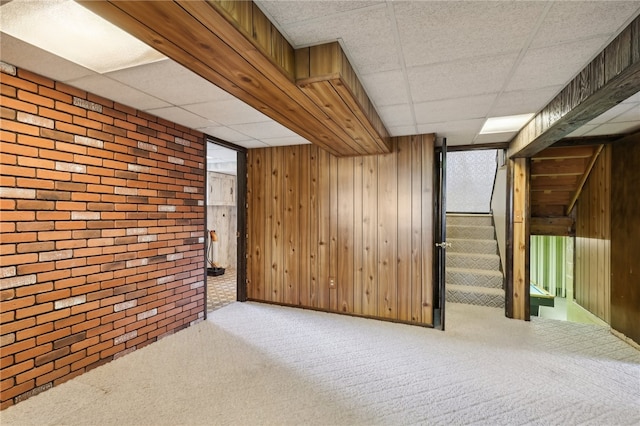 basement with a drop ceiling, brick wall, and carpet flooring