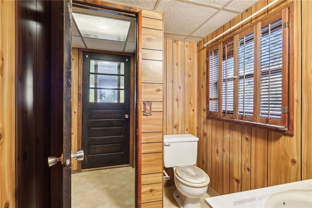 bathroom featuring sink, wooden walls, a drop ceiling, and toilet