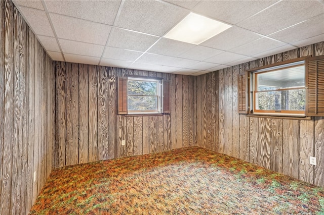 basement featuring wood walls, a paneled ceiling, and carpet flooring