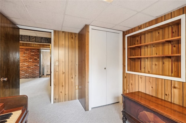 interior space with light carpet, a drop ceiling, and wooden walls