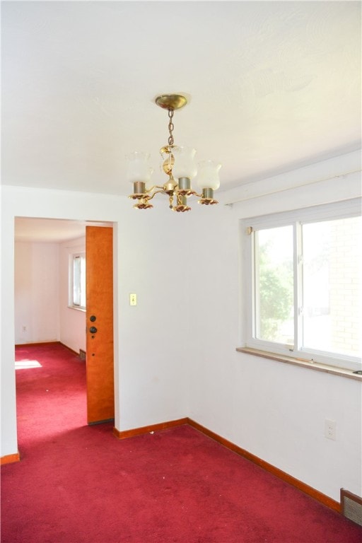 carpeted empty room featuring a healthy amount of sunlight and a notable chandelier