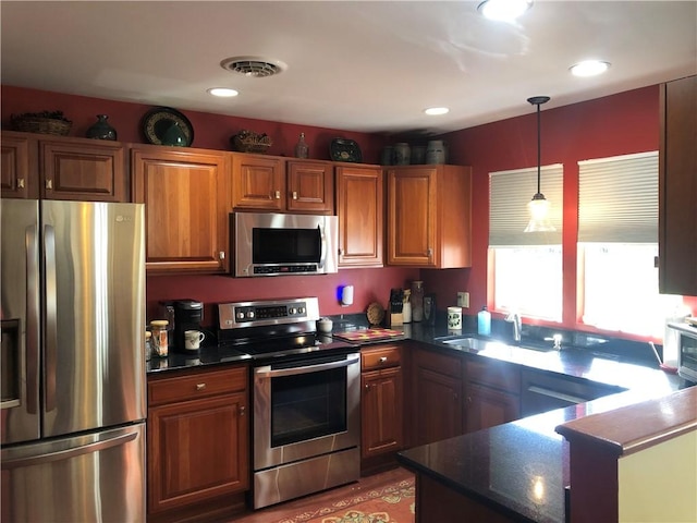 kitchen featuring a sink, appliances with stainless steel finishes, brown cabinets, and decorative light fixtures