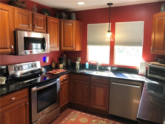kitchen featuring pendant lighting, appliances with stainless steel finishes, brown cabinetry, and a sink