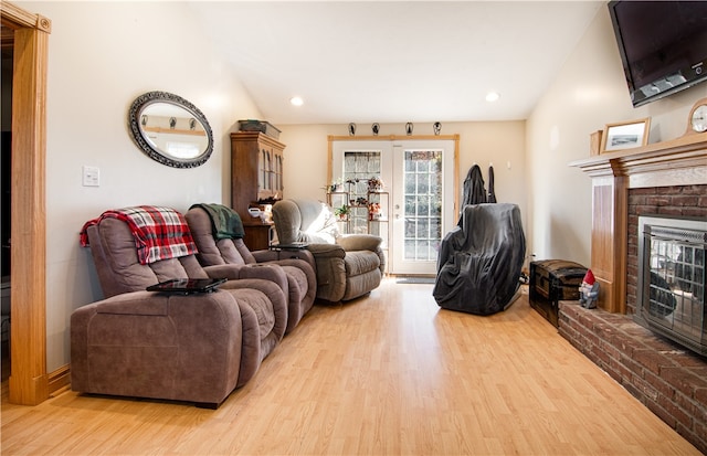 living room with french doors, light hardwood / wood-style floors, vaulted ceiling, and a brick fireplace