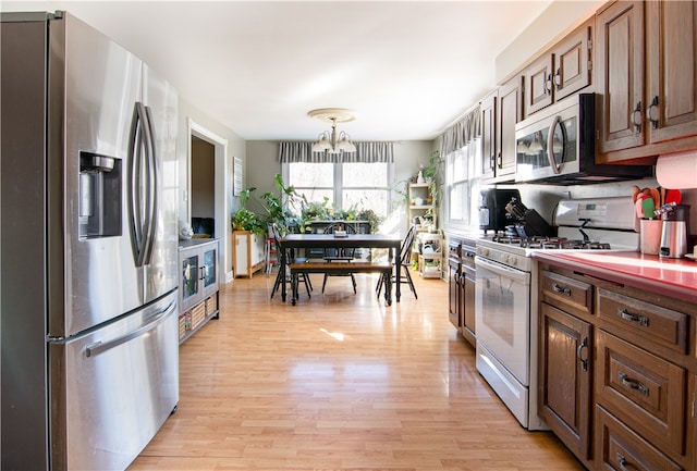 kitchen featuring an inviting chandelier, decorative light fixtures, stainless steel appliances, and light hardwood / wood-style floors