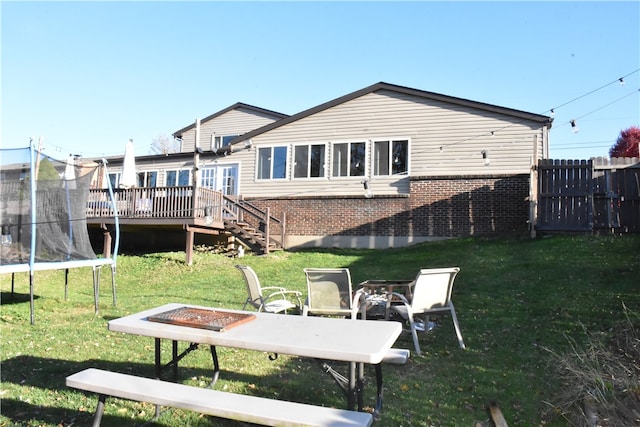 back of property featuring a lawn, a trampoline, and a deck