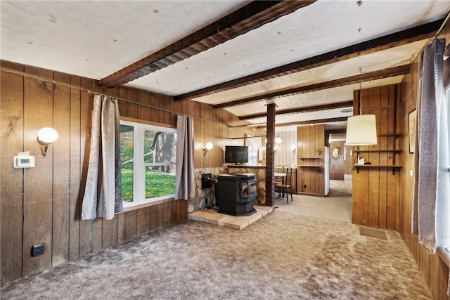 carpeted living room featuring beam ceiling, wood walls, and a wood stove