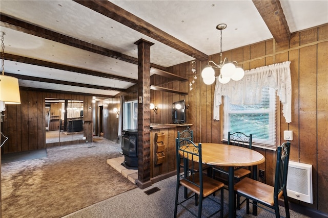 carpeted dining room with a wood stove, wood walls, beam ceiling, and a chandelier