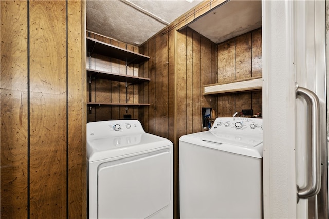 laundry area with independent washer and dryer, a textured ceiling, and wood walls