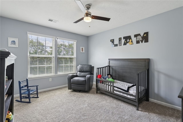 carpeted bedroom with ceiling fan, a textured ceiling, and a crib