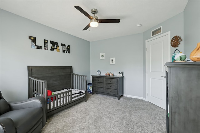 carpeted bedroom with a crib and ceiling fan