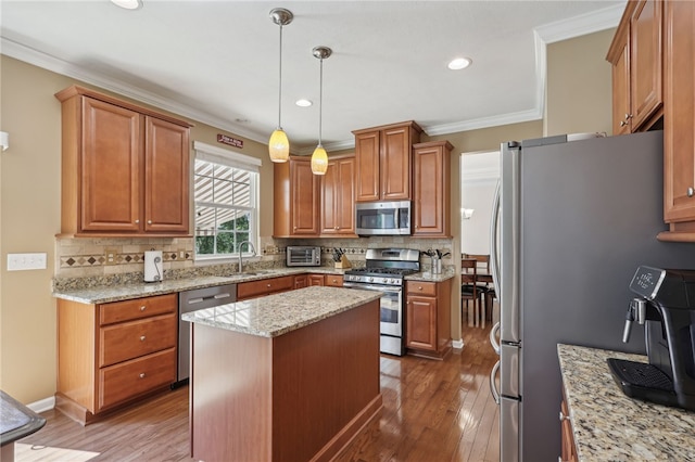 kitchen with hardwood / wood-style floors, hanging light fixtures, a kitchen island, appliances with stainless steel finishes, and sink