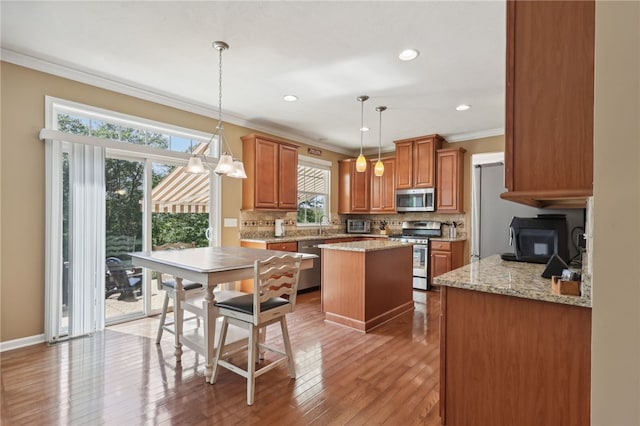 kitchen with decorative backsplash, stainless steel appliances, light stone countertops, pendant lighting, and light hardwood / wood-style floors