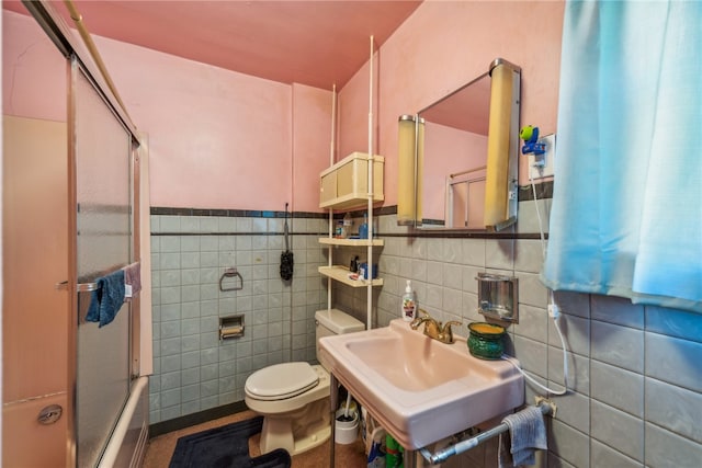 full bathroom with tile walls, sink, bath / shower combo with glass door, and toilet