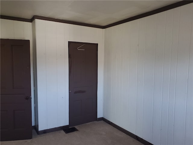 unfurnished room with ornamental molding, wood walls, and carpet flooring