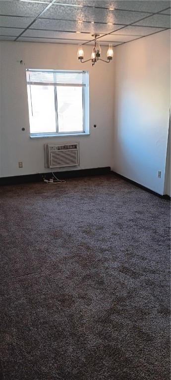 carpeted spare room featuring an AC wall unit and a drop ceiling