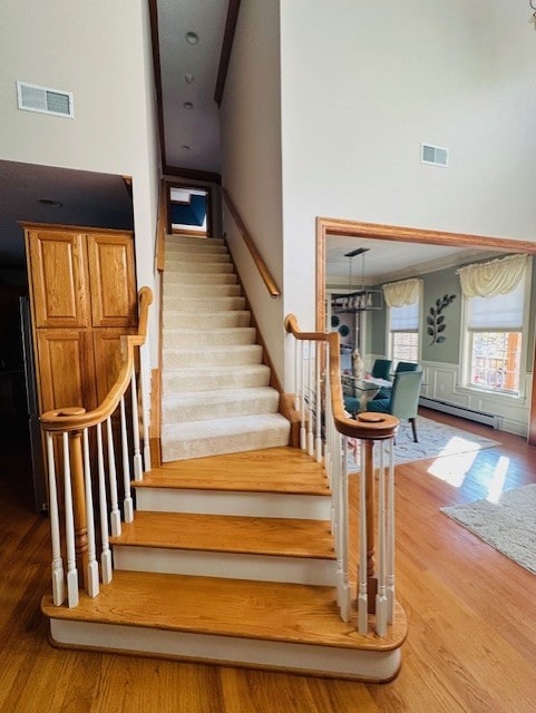 stairs featuring baseboard heating, wood-type flooring, and a high ceiling