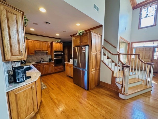 kitchen with appliances with stainless steel finishes, a towering ceiling, light wood-type flooring, backsplash, and ornamental molding